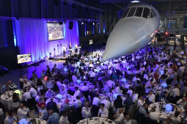 Arial shot of an awards ceremony with tables and chairs and a stage placed under a Concorde plane